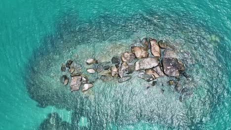 Aerial-top-down-view-of-small-coral-reef-and-rocks-in-blue-sea