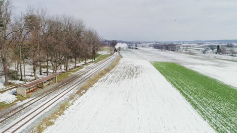 Ariel-Blick-Auf-Eine-Dampflokomotive-Und-Personenkraftwagen,-Die-Nach-Dem-Ersten-Schnee-Der-Saison-über-Amish-Ackerland-Schnaufen