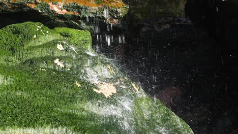 Zeitlupe-Eines-Kleinen-Wasserfalls,-Der-Auf-Einen-Moosgrünen-Felsen-Prasselt