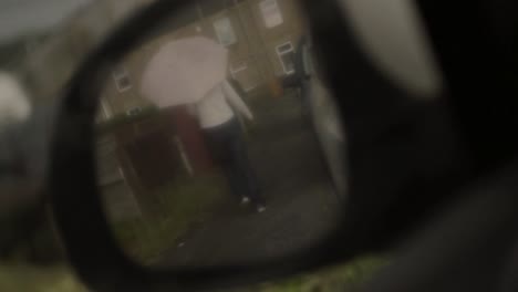 Woman-with-umbrella-in-the-rain-pov-of-rear-view-mirror