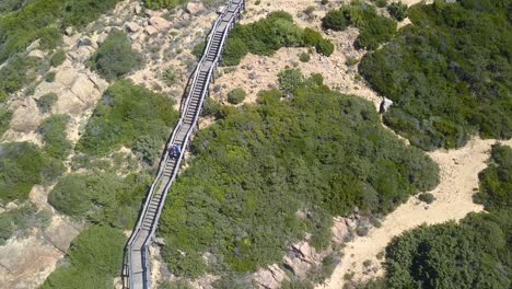 Aerial-shot-following-a-couple-going-up-on-a-wooden-walkway-in-a-cape-in-a-beach-of-the-south-of-Spain