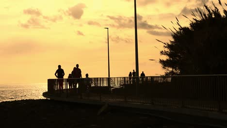 Unidentifiable-People-walking-in-silhoutte-on-a-bridge-late-afternoon-seaside-sunset-warm-colors