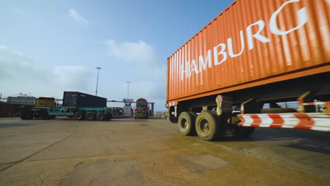 Trucks-entering-into-the-port,-A-long-vehicle-container-traller-is-moving-on-the-road-of-a-port,-camera-passing,-close-up-view