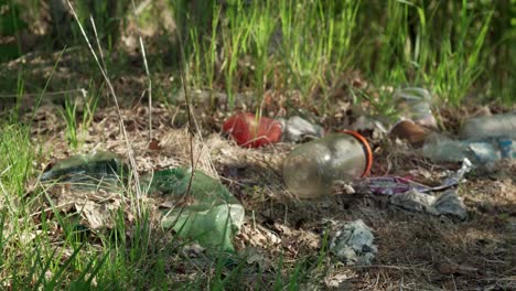 Garbage-in-nature---illegal-dump-full-of-plastic-and-glass-trash,-grass-and-trees-in-the-background,-close-up