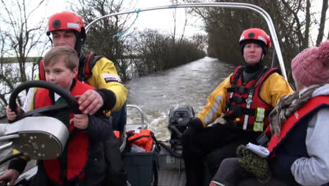 Großbritannien,-Februar-2014-–-Ein-Feuerwehrmann-Lässt-Einen-Kleinen-Jungen-Ein-Boot-Steuern,-Mit-Dem-Bewohner-In-Das-Vom-Hochwasser-Abgeschnittene-Dorf-Muchelney-Transportiert-Werden