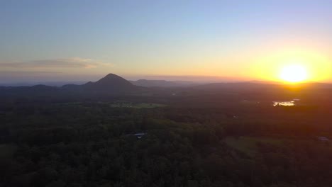 Luftaufnahme-Eines-Atemberaubenden-Goldenen-Sonnenuntergangs-An-Der-Sonnenscheinküste-Mit-Wäldern-Und-Bergen