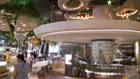 Kaskadierende-Lichterketten-Hängen-über-Die-Etagen-Des-Icon-Siam-Luxus-Einkaufszentrums,-Während-Menschen-Im-Vordergrund-Vorbeigehen