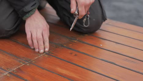 Hands-young-carpenter-using-knife-to-remove-old-mastic-from-planking