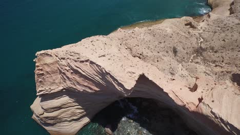 Aerial-shot-of-stunning-rock-formation-and-a-vulture-flying-in-Punta-Colorada,-Sea-of-Cortez