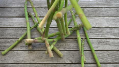 Slow-motion-footage-of-a-bunch-of-fresh,-green-asparagus-falling-on-to-a-wood-table