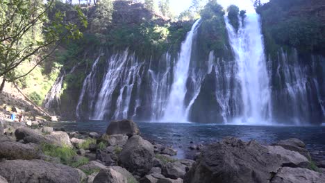 4K-footage-of-Burney-Falls,-with-a-man-swimming-in-and-out-of-the-freezing-cold-water-on-the-left-bottom-corner