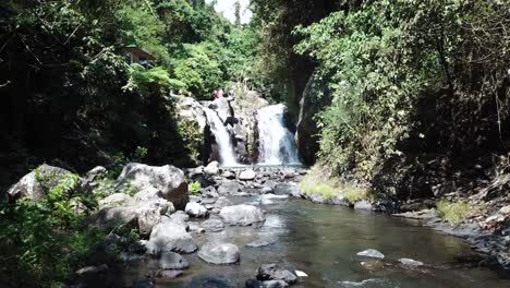 Drohnenschuss,-Der-Auf-Einen-Der-Alingaling-Wasserfälle-In-Bali,-Indonesien,-Zufliegt,-Während-Man-Touristen-Herumlaufen-Sehen-Kann