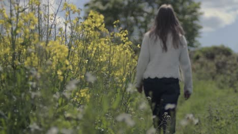 Carefree-woman-walking-through-field-of-rapeseed-in-countryside-landscape