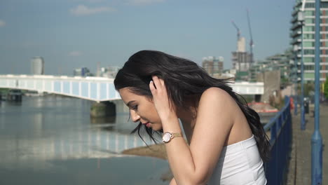 Beautiful-latina-woman-on-holiday-leaning-against-the-railing,-looking-down-at-the-river-Thames-in-London