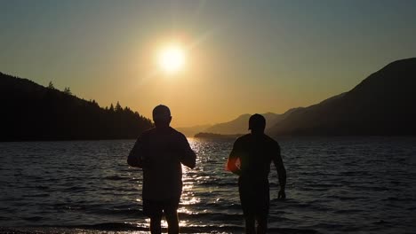 Sunset-on-a-lake-with-mountains-in-the-background-with-two-guys-having-a-drink-in-Silhouette