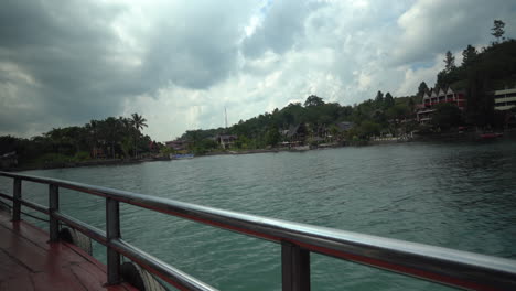 Aufnahmen-Einer-Fähre,-Die-über-Den-Toba-See-In-Nord-Sumatra,-Indonesien,-Fährt-Und-An-Traditionellen-Seeresorts-Im-Batak-Stil-Vorbeifährt