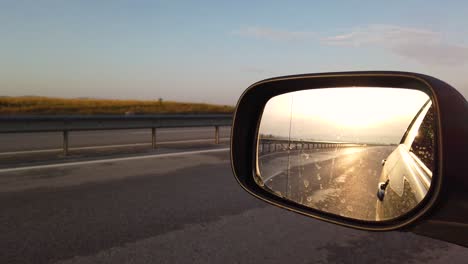 Reflection-side-rear-view-car-mirror-in-the-morning-on-the-road-at-sunset-or-sunrise