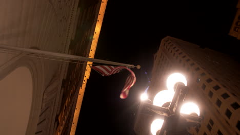 Bandera-Estadounidense-Colgada-En-Un-Edificio-Al-Lado-De-Una-Lámpara-De-Calle-Vintage-Y-En-Movimiento