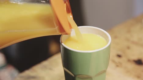 Close-up-of-orange-juice-being-poured-into-a-porcelain-cup