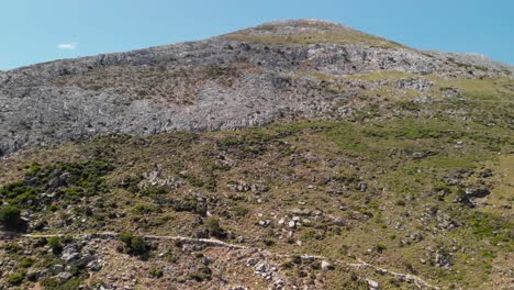 Antena-De-Ascenso-Lento-Sobre-Una-Montaña-Rocosa-Y-árida-Con-Camino-Y-Cielo-Azul