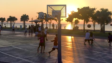 Teenager-Spielen-Abends-Bei-Sonnenuntergang-Auf-Den-Plätzen-Am-Meer-Basketball