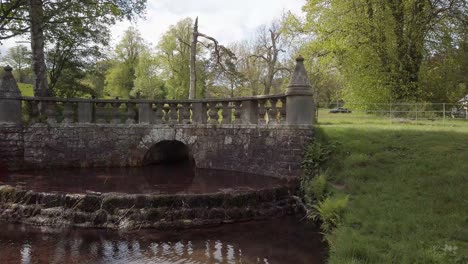 Characterful-ornate-bridge-in-country-walk-in-Fife-Scotland-with-small-stream-under-cascading-into-pond
