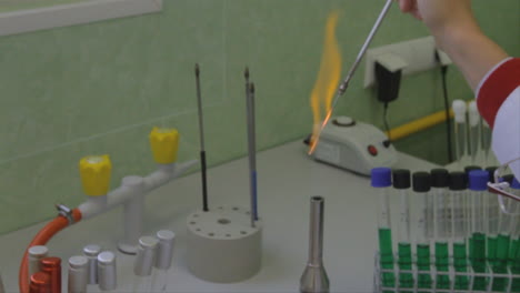 In-Einem-Wissenschaftlichen-Labor-Entsteht-Eine-Bunte-Orangefarbene-Flamme,-Wenn-An-Einer-Dünnen-Pipette,-Die-Der-Wissenschaftler-über-Eine-Offene-Flamme-Hält,-Eine-Chemische-Reaktion-Stattfindet