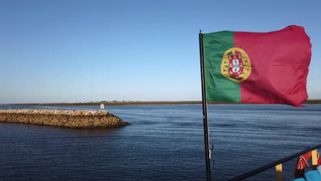 Portuguese-flag-flaps-in-strong-wind-on-ferry-in-Olhao-harbor,-Portugal