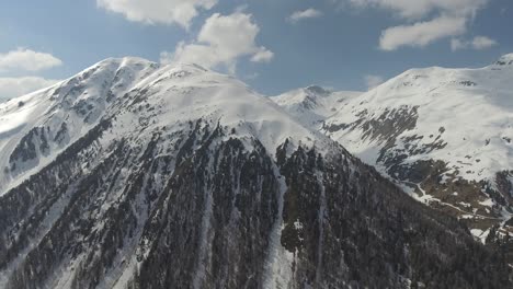 Aerial-shot-of-steep-slope-and-snowy-peak-in-italian-alpes,-reveal-of-a-pass