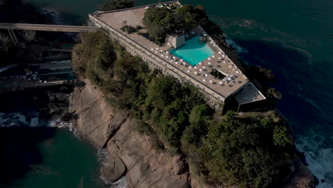 Luftaufnahme-Des-Swimmingpools-Auf-Dem-Dach-Mit-Sonnenschirmen,-Die-Den-Blick-Auf-Die-Insel-Freigibt,-Auf-Der-Das-Bauwerk-Errichtet-Wurde,-Sowie-Auf-Die-Weitere-Küstenlandschaft-Von-Rio-De-Janeiro