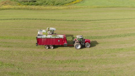 4K-aerial-view-panning-right-of-a-harvester-harvesting-hay-into-a-tractor-and-wagon