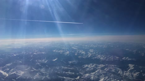 footage-from-an-airplane-showing-an-airplane-white-trail-flying-far-away-and-snowy-mountains-from-above-the-Alps-in-Europe-2