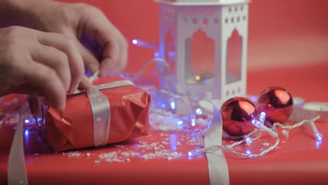 Wrapping-Christmas-gift-with-ribbon-and-red-paper-with-red-background-and-baubles
