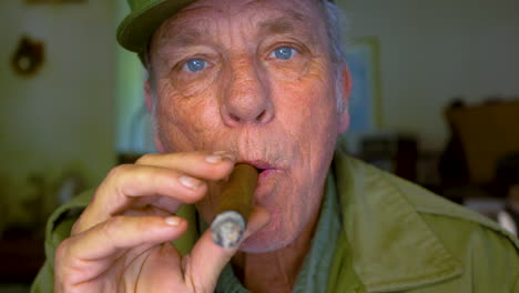 Mature-male-in-his-60s-blowing-cigar-smoke-directly-at-the-camera
