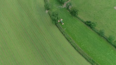Top-down-aerial-of-a-tractor-mowing-a-narrow-field-inbetween-much-larger-fields