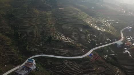 Aerial-view-tiltup-to-reveal-amazing-rice-terraced-green-misty-mountainside-and-winding-road-in-Sapa,-Vietnam-at-dusk-as-sun-sets