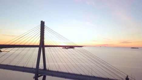 Aerial,-Beautiful-summer-scenery-in-Finland,-cable-stayed-bridge-lit-up-by-orange-sunset