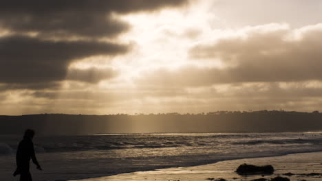 Waves-Break-In-Slow-Motion-On-Coronado,-California,-Beach-At-Sunset-As-Person-Walks-Through-Frame