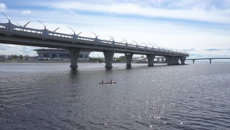 Aerial-Drone-tracking-Shot-of-two-people-riding-a-kayak-under-the-Western-High-Speed-Diameter-bridge,-Gulf-of-Finland-in-Saint-Petersburg,-Russia