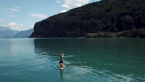 Aerial,-drone-shot-of-a-stand-up-paddler-on-a-yellow-sup,-stand-up-paddle,-in-the-middle-of-a-fjord-lake-in-Switzerland-while-summer