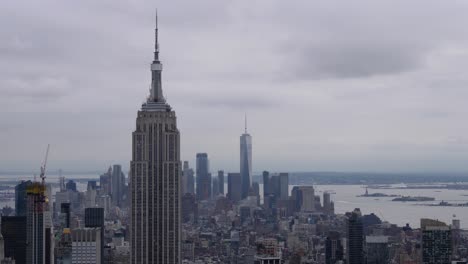 Time-Lapse-of-clouds-over-the-Empire-State-Building-and-One-World-Trade-Center,-and-boat-traffic-on-Hudson-River-in-the-background-which-leads-to-the-Island-of-Liberty-in-New-York-City,-June-2019