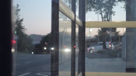 Point-of-view-of-urban-city,-traffic-at-dusk-through-bus-stop-windows