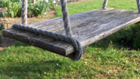 LOCKED-OFF-view-of-wooden-swing-seat-gently-swaying-in-the-wind
