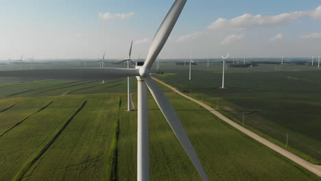 Drone-flying-away-from-an-up-close-shot-of-a-wind-turbine-nose-cone-to-show-a-field-of-wind-generators