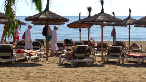 4k-elderly-couple-looking-for-sun-beds-on-the-beach-in-marbella,-malaga,-spain,-costa-del-sol-holiday
