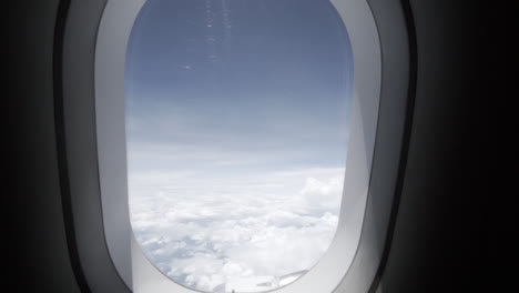 Slow-motion-dolly-pull-in-of-an-airplane-window-while-in-flight-withe-a-nice-blue-sky-and-white-clouds