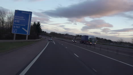 Toma-En-Movimiento-De-Un-Vehículo-Que-Conduce-Por-La-Carretera-Con-Otro-Tráfico-Con-Maravillosa-Luz-De-Puesta-De-Sol-Y-Nubes-En-Edimburgo,-Escocia
