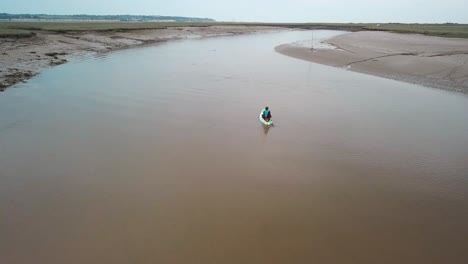 Man-kayaking-on-meandering-river,-drone-follows-behind-and-then-flies-over,-camera-pans-down
