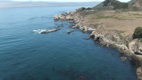 Up-reveal-aerial-of-Notleys-Landing-Viewpoint-of-the-Pacific-Ocean-crashing-waves-on-the-rocky-cliffs-near-Highway-1-in-California,-USA