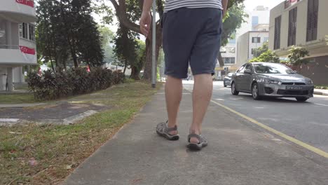 Lower-view-of-the-man-wearing-short-and-adventure-sport-sandal-while-walking-on-the-pathway-in-singapore-area-in-daytime-with-some-cars-on-the-street